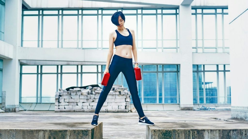 woman wearing black sports bra and pants while holding two red weights